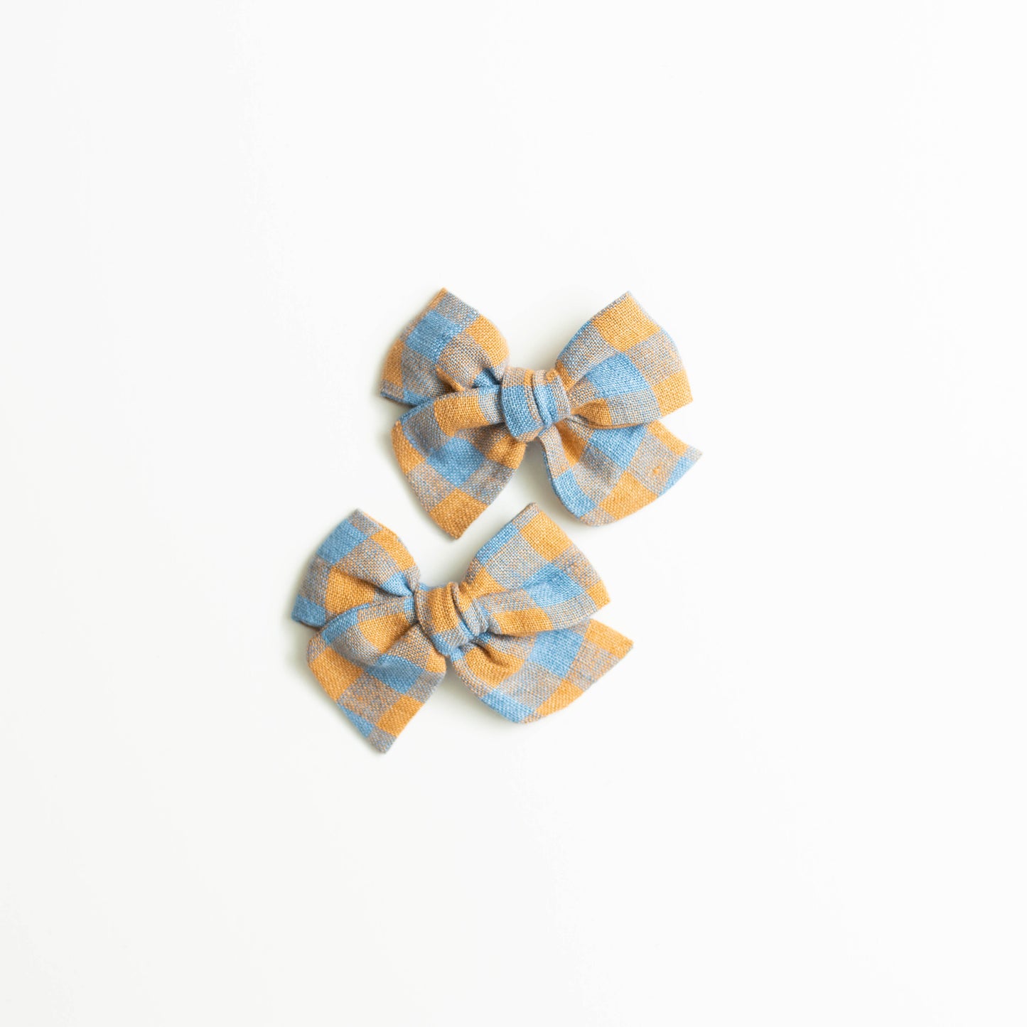 The Explorer and Scarecrow fabric bows from Shop Acre Goods, featuring a blue and orange checkered pattern, are elegantly attached to nylon headbands against a plain white background.