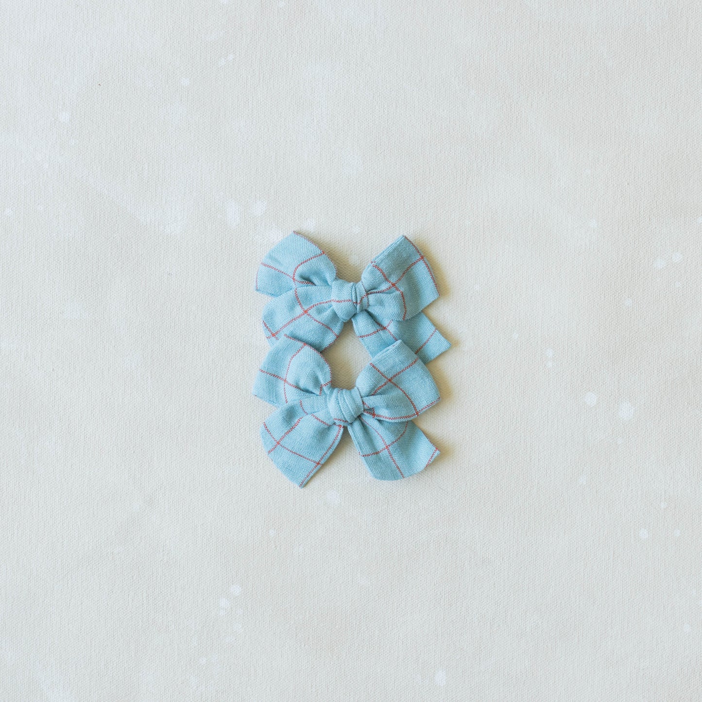The Explorer // Hopscotch set by Shop Acre Goods features two light blue, checkered hair bows with a classic tied design on an off-white background. Perfect for piggy sets, each bow is symmetrically arranged and secured with an alligator clip at the knot.