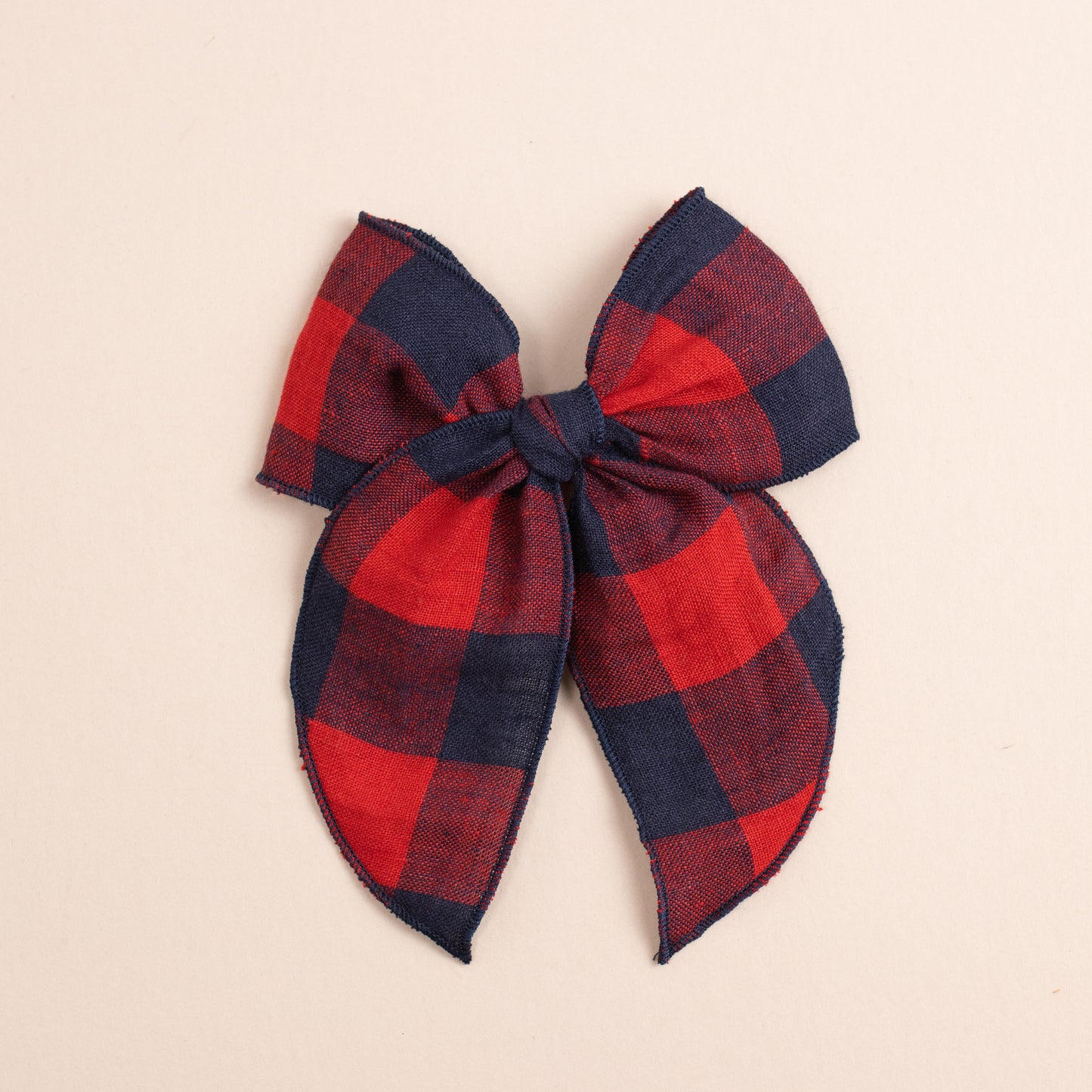 The Fleur // Game Day bow by Shop Acre Goods features a large red and blue plaid linen design with frayed edges, set on a plain light background, and is secured with a sturdy alligator clip.