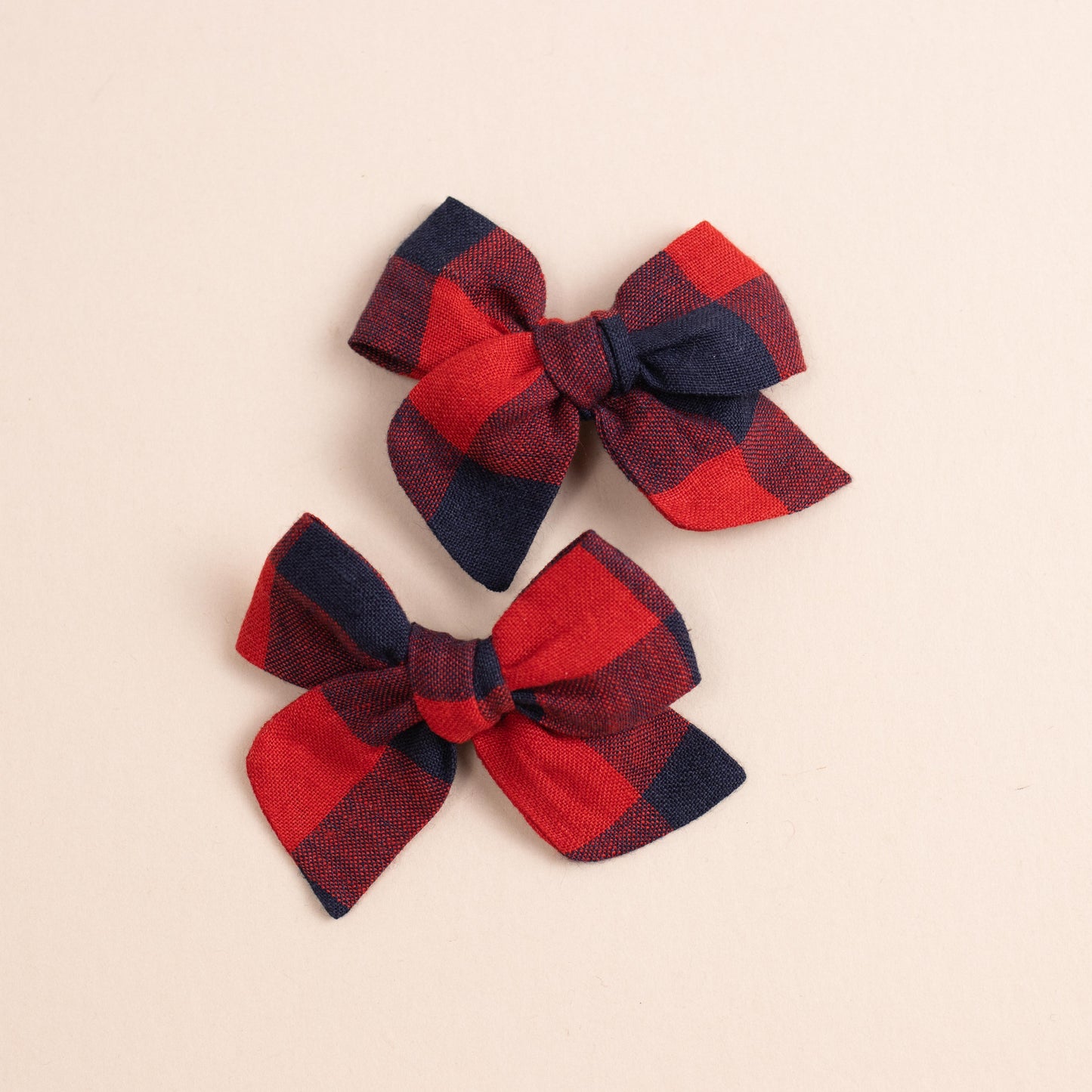 Two red and black checkered fabric bows from Shop Acre Goods Explorer // Game Day collection are set against a light beige background. Their simple and symmetrical design adds an elegant touch to this charming piggy set.