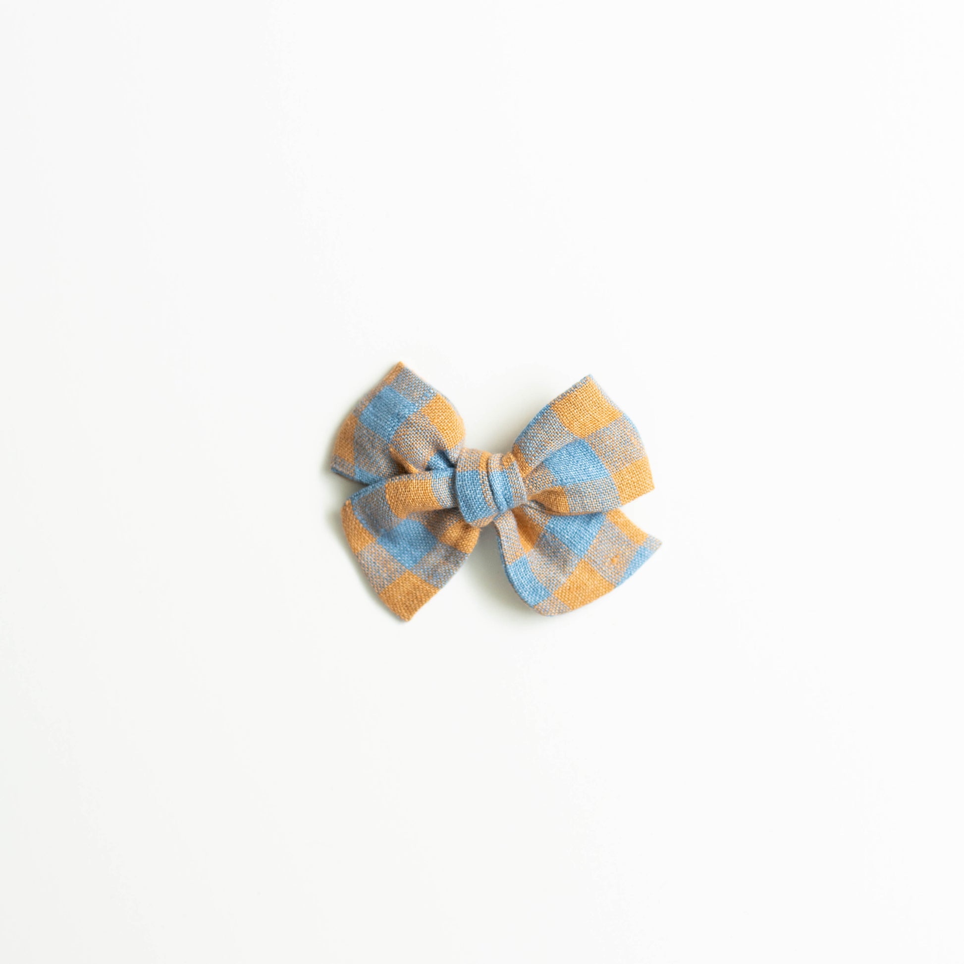 The Explorer // Scarecrow by Shop Acre Goods features an elegant orange and blue plaid fabric bow on an alligator clip, displayed against a white background.