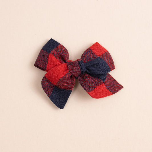 The Shop Acre Goods Explorer // Game Day features a fabric bow with a red and navy checkered pattern, neatly tied on a reversible alligator clip, against a light beige background.